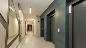 A modern hotel corridor with a long hallway, elevators, and a clean, tiled floor.