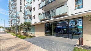 A modern building with a glass entrance, numbered 31, and a paved walkway with greenery.