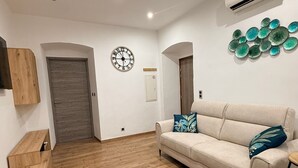 Uma sala de estar com piso de madeira, um sofá bege, uma mesa de centro redonda e um ar condicionado fixado na parede.