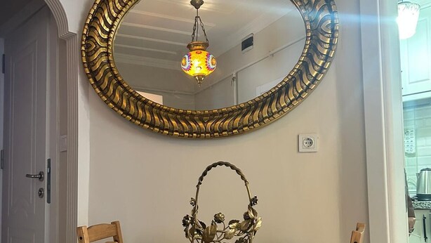 A dining area with a round wooden table, two chairs, a decorative mirror, and a hanging light fixture. - Bohemian Antique House in Colorful Balat (İstanbul)