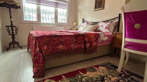 A bedroom with a bed, a chair, a window with blinds, a lamp, and a painting on the wall. - Bohemian Antique House in Colorful Balat (İstanbul)