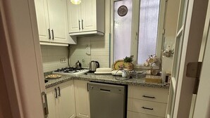 A compact kitchen with white cabinets, a gas stove, a dishwasher, and patterned floor tiles. - Bohemian Antique House in Colorful Balat (İstanbul)