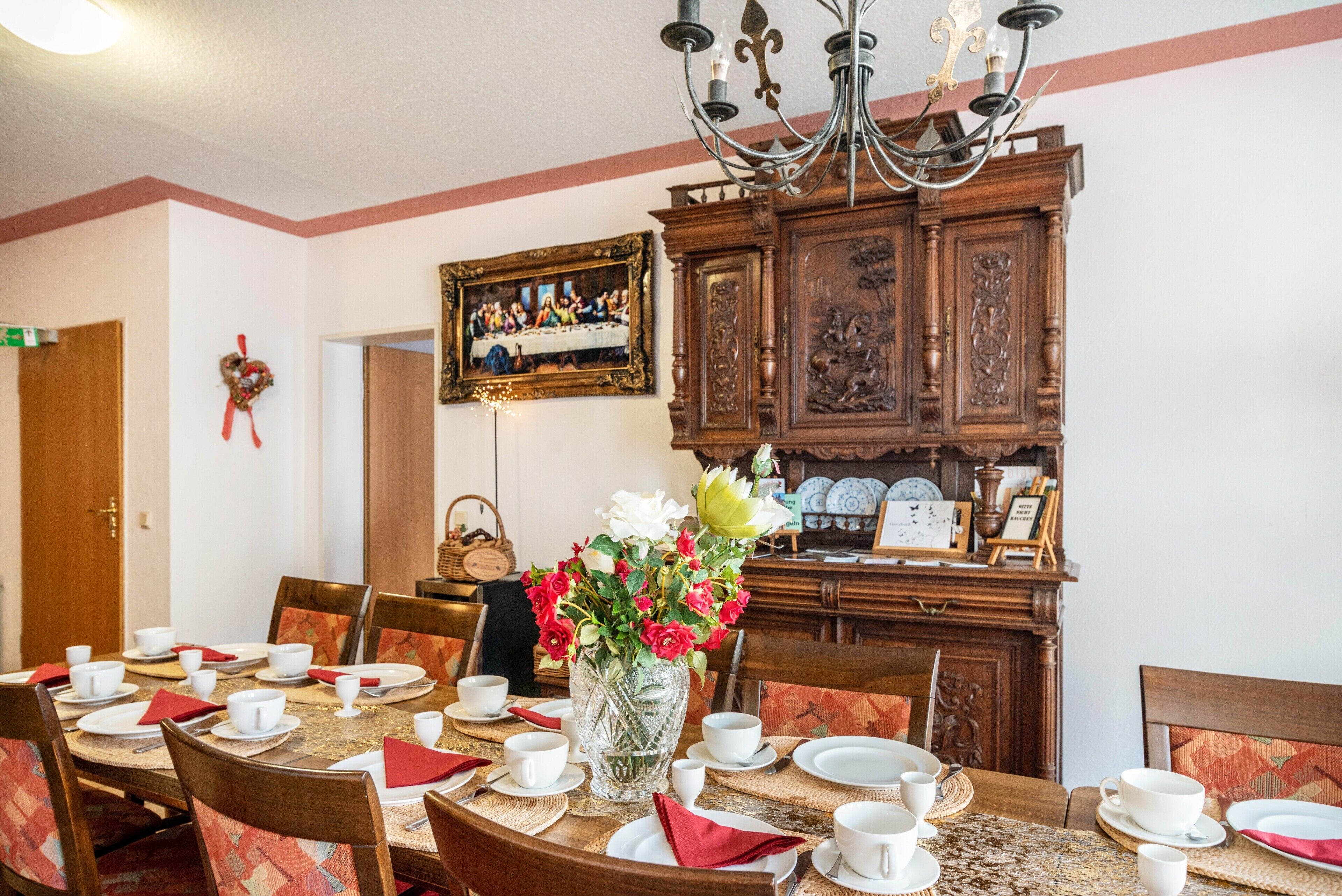 A dining area with a table set for four, a chandelier, and a wooden cabinet with decorative items.
