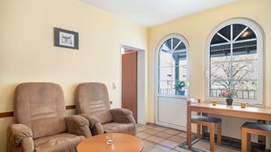 A room with two leather armchairs, a small wooden table, a dining table with chairs, a window with an arched design, and a framed picture on the wall. - Apartment "Ferienwohnung 2" with Balcony, Moselle & Mountain Views, Shared Terrace, and Wi-Fi (Bernkastel-Kues)
