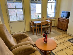 A living room with a sofa, a dining table with chairs, a small table with a vase, and a TV on a cabinet.