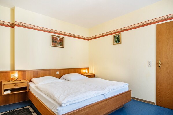 A hotel room with a wooden bed, two bedside tables with lamps, a door, and a wall with a decorative border.