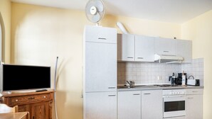 A compact kitchen with a refrigerator, stove, sink, and a television on a wooden cabinet. - Apartment "Ferienwohnung 2" with Balcony, Moselle & Mountain Views, Shared Terrace, and Wi-Fi (Bernkastel-Kues)