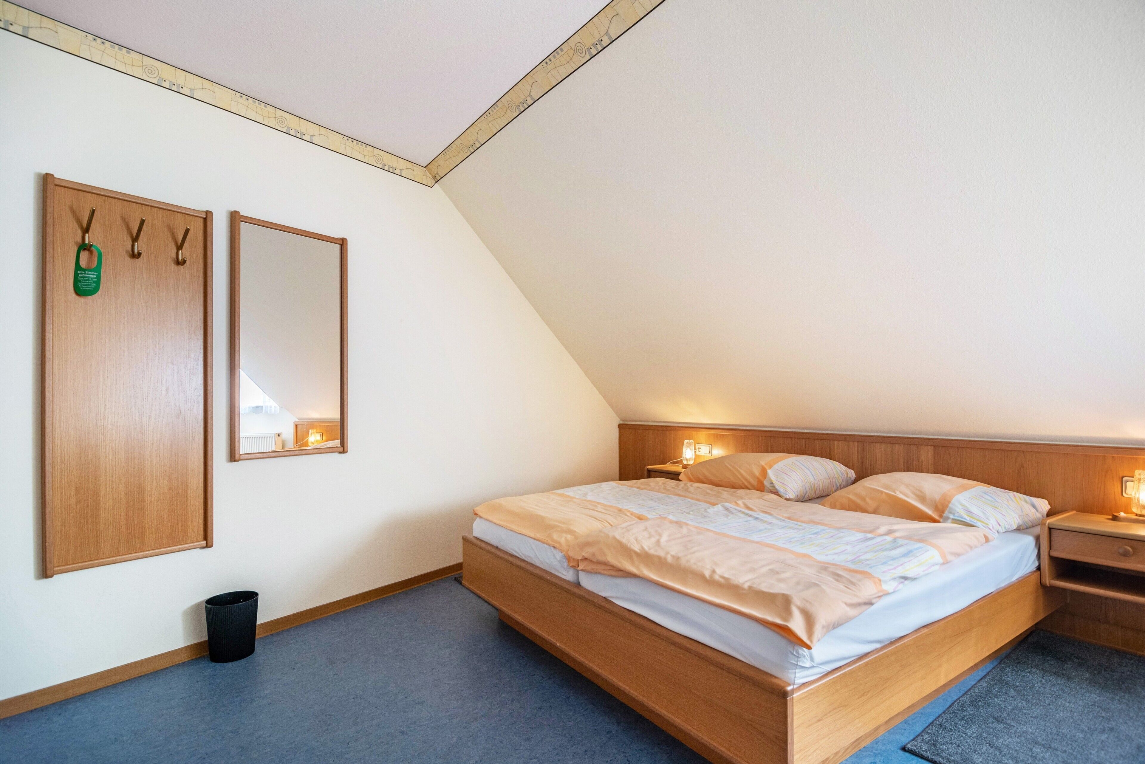 Ein Schlafzimmer mit einem hölzernen Bett, einem Nachttisch, einem wandmontierten Spiegel und einer Mülltonne.