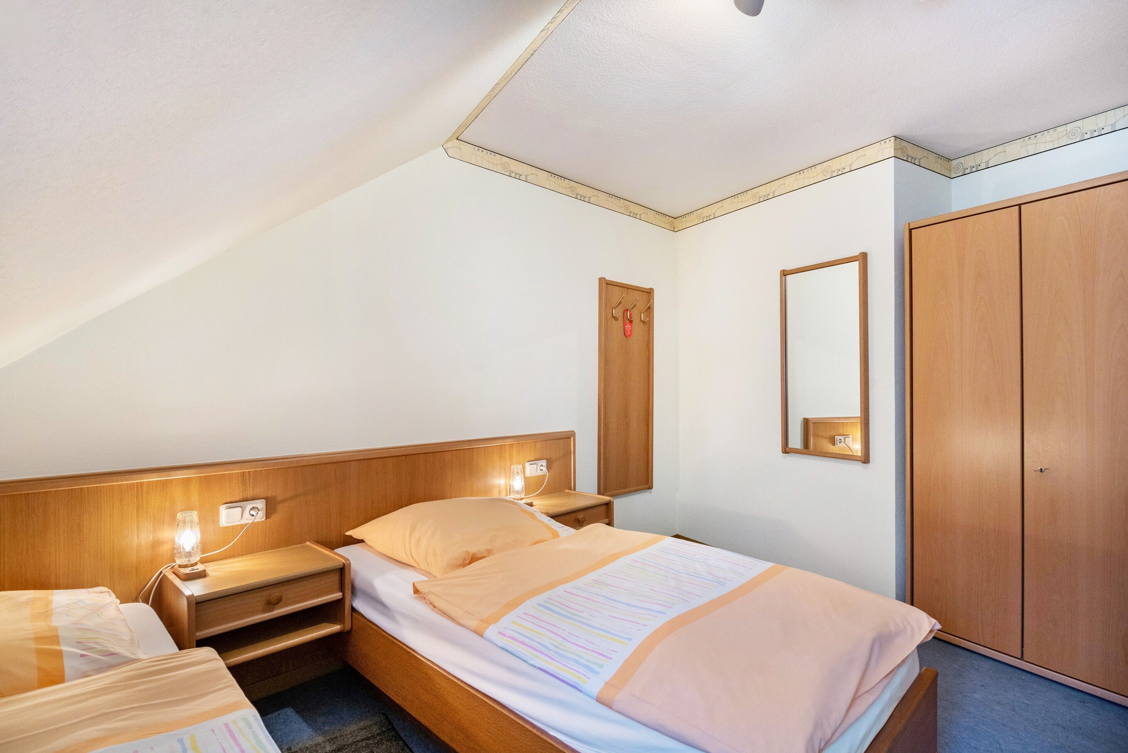 Une chambre d’hôtel avec deux lits, des têtes de lit en bois, des lampes de chevet, une armoire et un miroir.