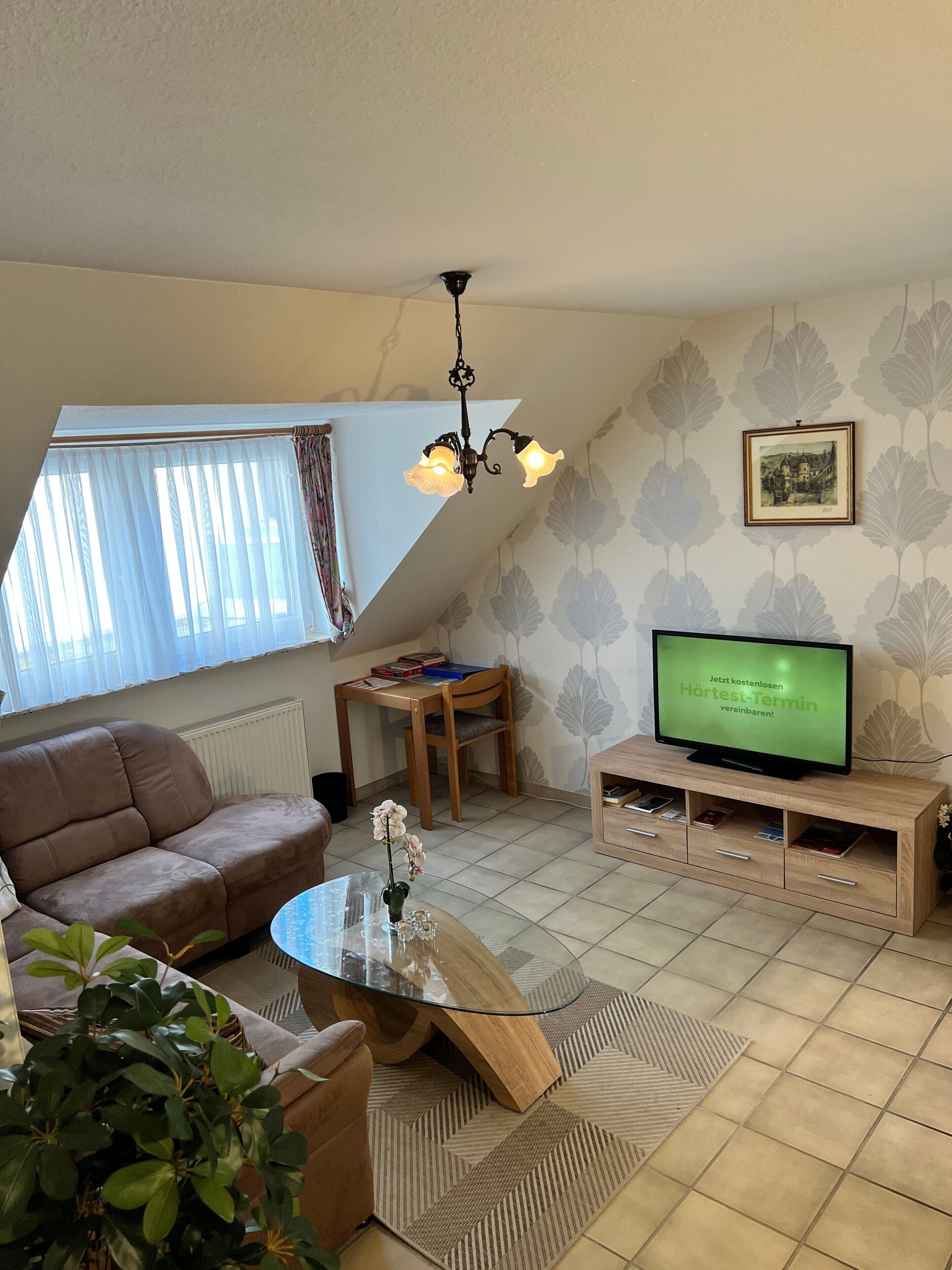 Una sala de estar con sofá, una mesa de centro de vidrio, televisor y pared con diseño.