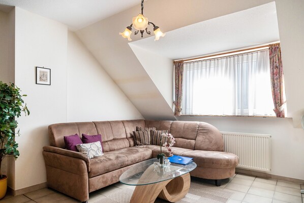 A living room with a brown leather sofa, a glass coffee table, a potted plant, a picture on the wall, and a window with curtains.