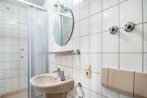 A bathroom with a sink, mirror, shower, and tiled walls.