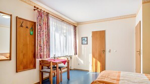 Ein Schlafzimmer mit einem Bett, einem Holzstuhl, einem Tisch, einem Fenster mit Vorhängen und einer Tür.