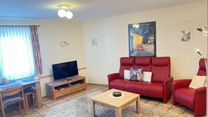 Ein Wohnzimmer mit rotem Sofa, Fernseher, kleinem Tisch und einem Gemälde an der Wand.