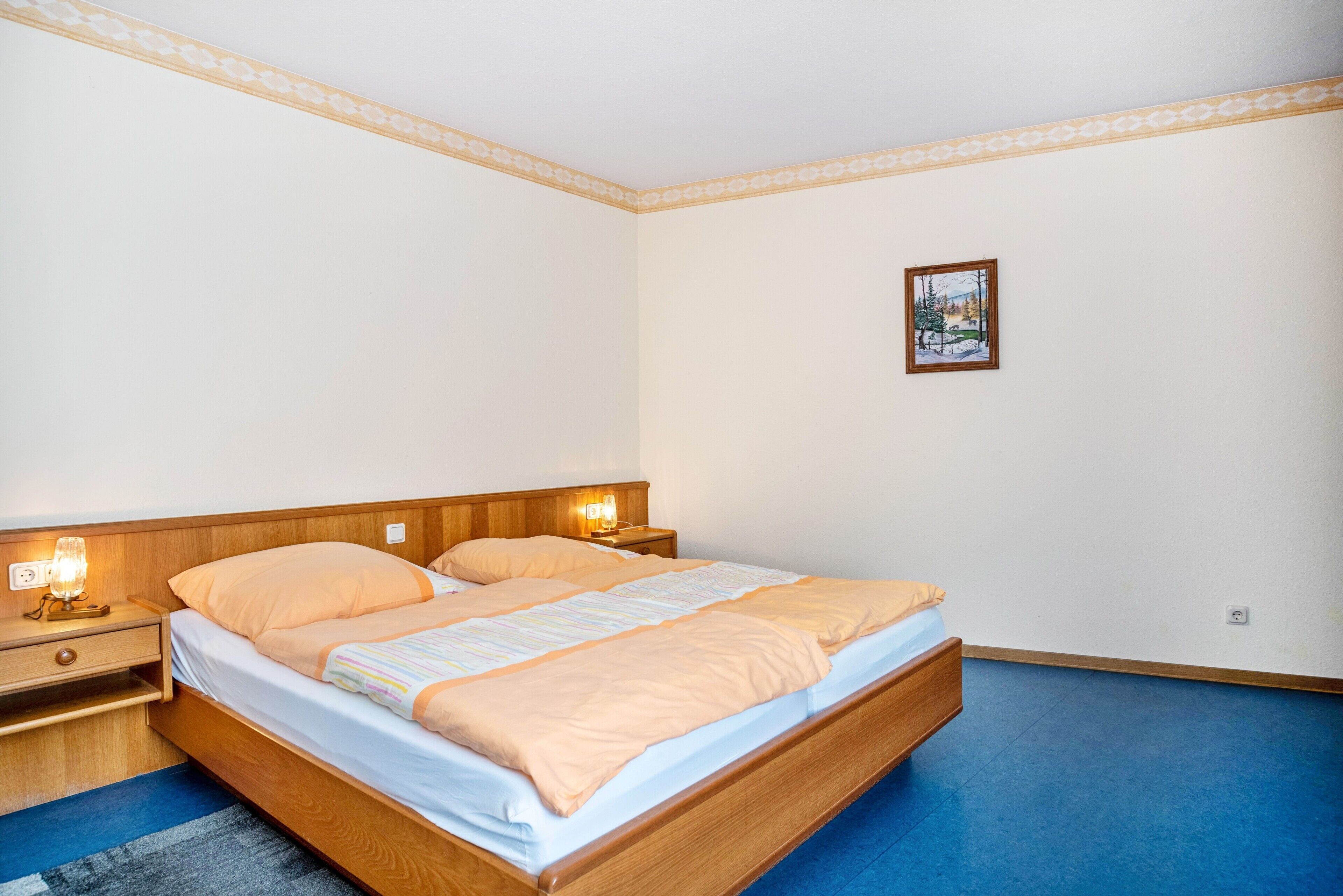 Une chambre à coucher avec un lit en bois, deux tables de chevet avec des lampes, un tableau encadré au mur et un tapis bleu.