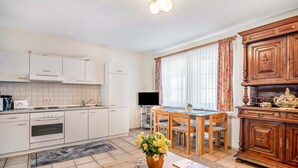 Eine moderne Küche mit weißen Schränken, ein Essbereich mit Holzsesseln und ein Holzschrank mit Dekorationselementen.