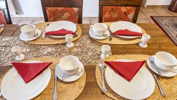 A dining table set with plates, bowls, cups, and cutlery, arranged on woven placemats.