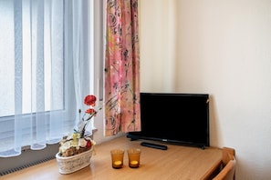 Habitació amb televisió, taula de fusta, un ram de flors i finestra amb cortines translúcides.