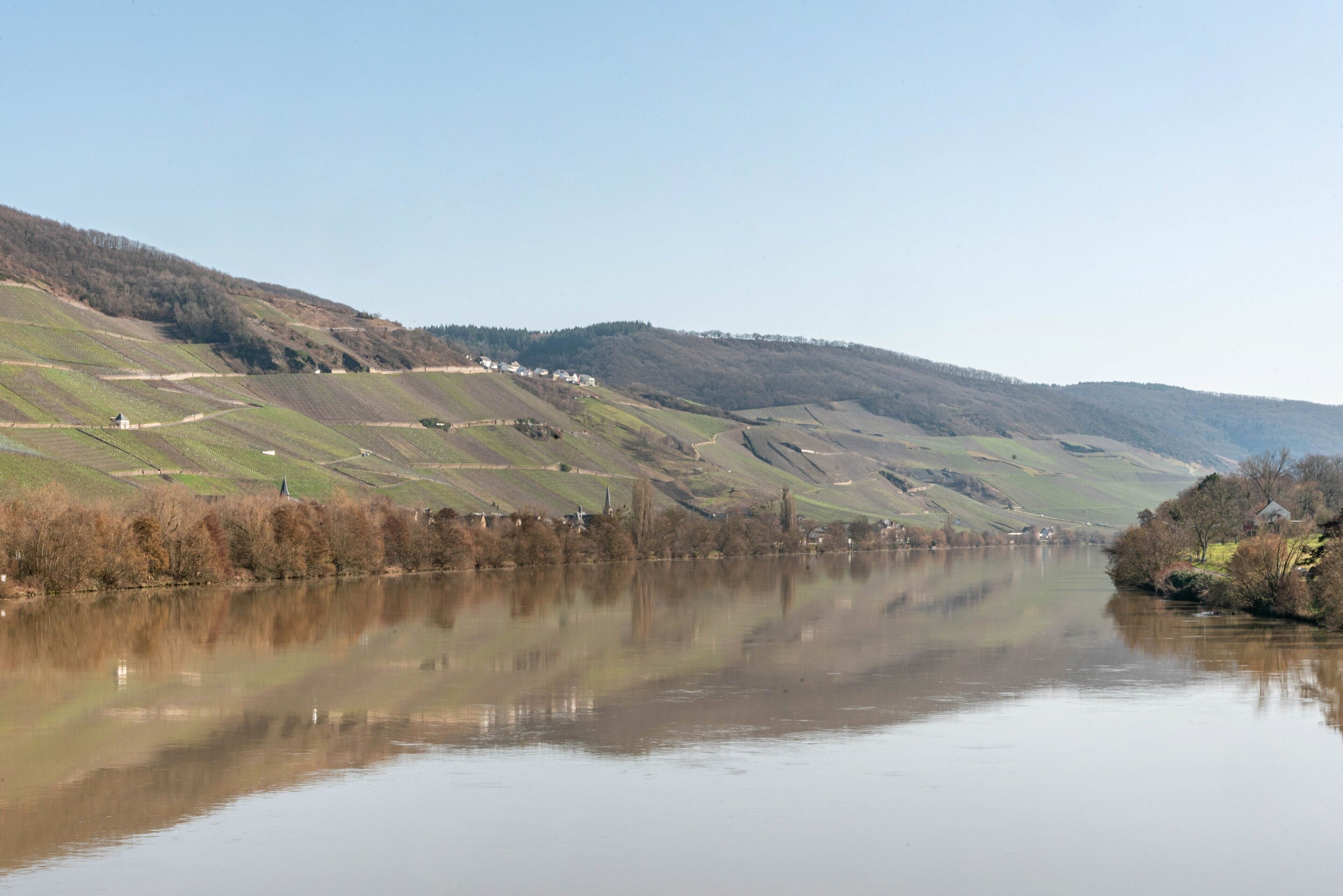 Une rivière à la surface calme, qui reflète le paysage environnant, notamment les collines et la végétation clairsemée.