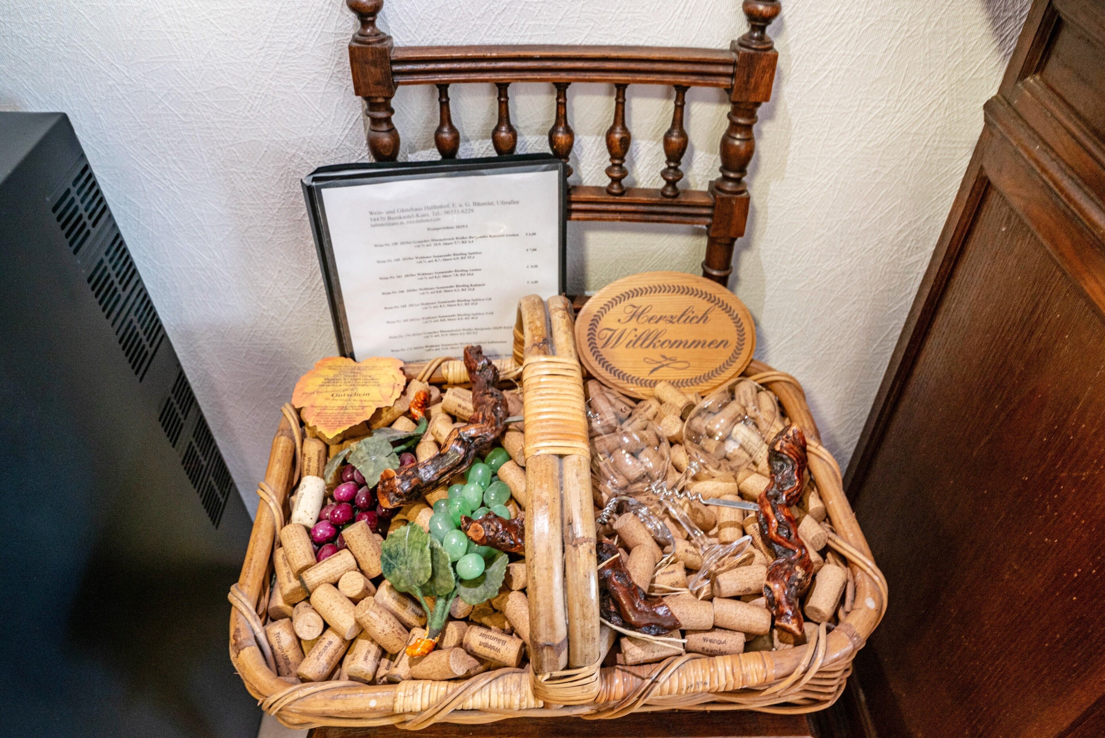 A wicker basket filled with various items including corks, a wooden spoon, and a wooden plaque with text.