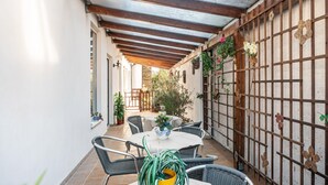 Een overdekt terras met een tafel, stoelen, een houten poort en potplanten.