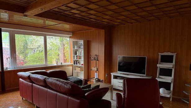 Un soggiorno con un divano, una TV, una libreria e una finestra con vista sugli alberi.