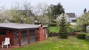 Un edificio in mattoni con ampie finestre e un camino, circondato da un prato curato e un alto abete sempreverde.
