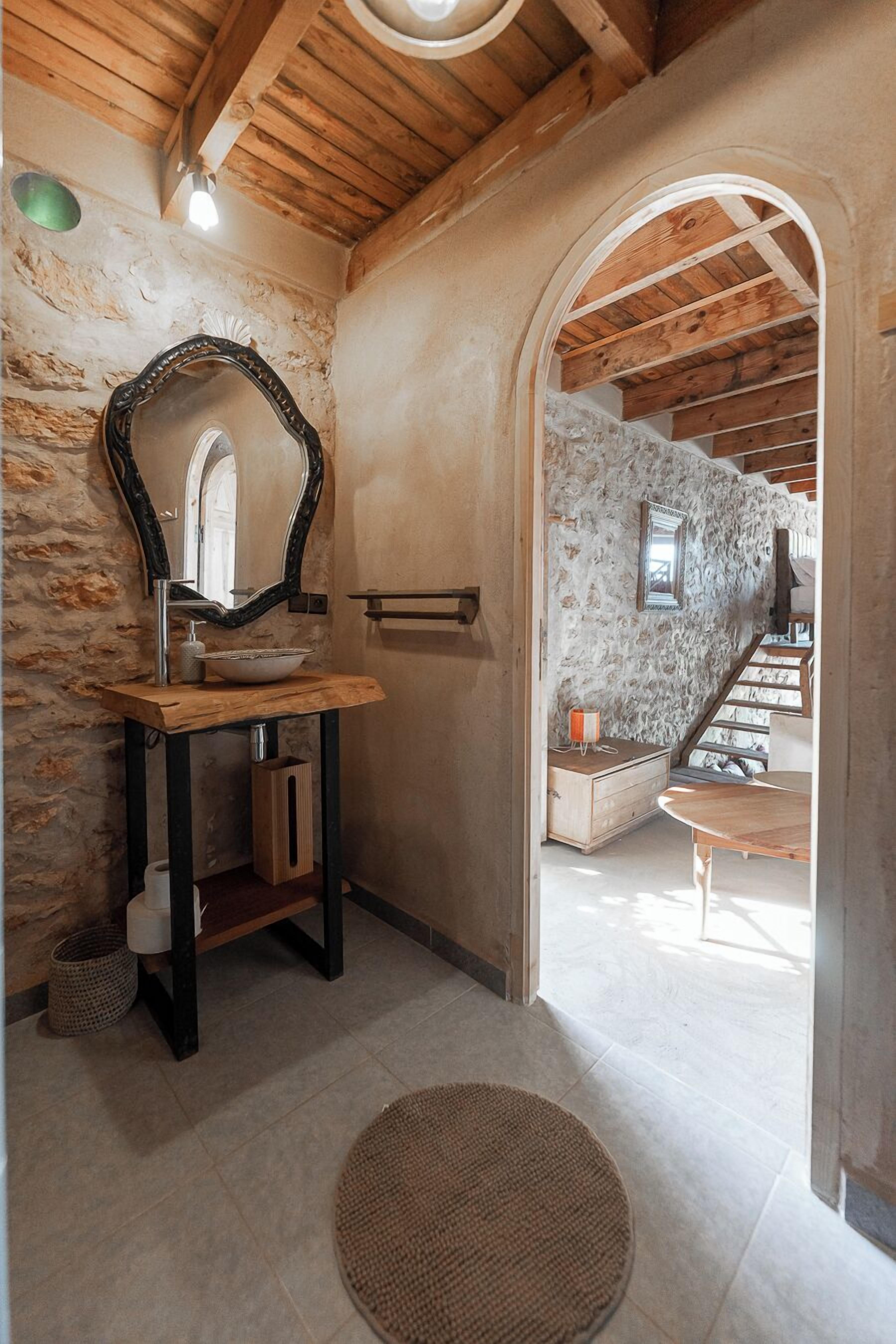 A rustic bathroom with a wooden vanity, a large mirror, and a stone wall.