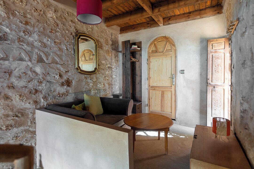A rustic room with stone walls, a wooden ceiling, a sofa, a table, and a wooden door.