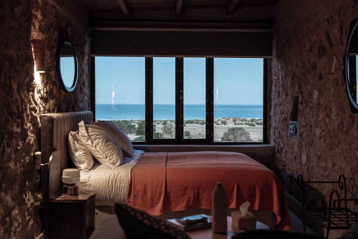 A bedroom with a large window, a bed with pillows, a bedside table, and a nightstand.