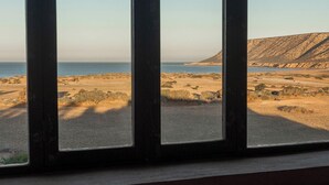 Una habitación con un amplio ventanal con vistas a una playa y un paisaje montañoso.
