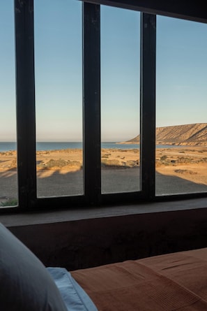 A room with a large window overlooking a beach and a mountainous landscape.