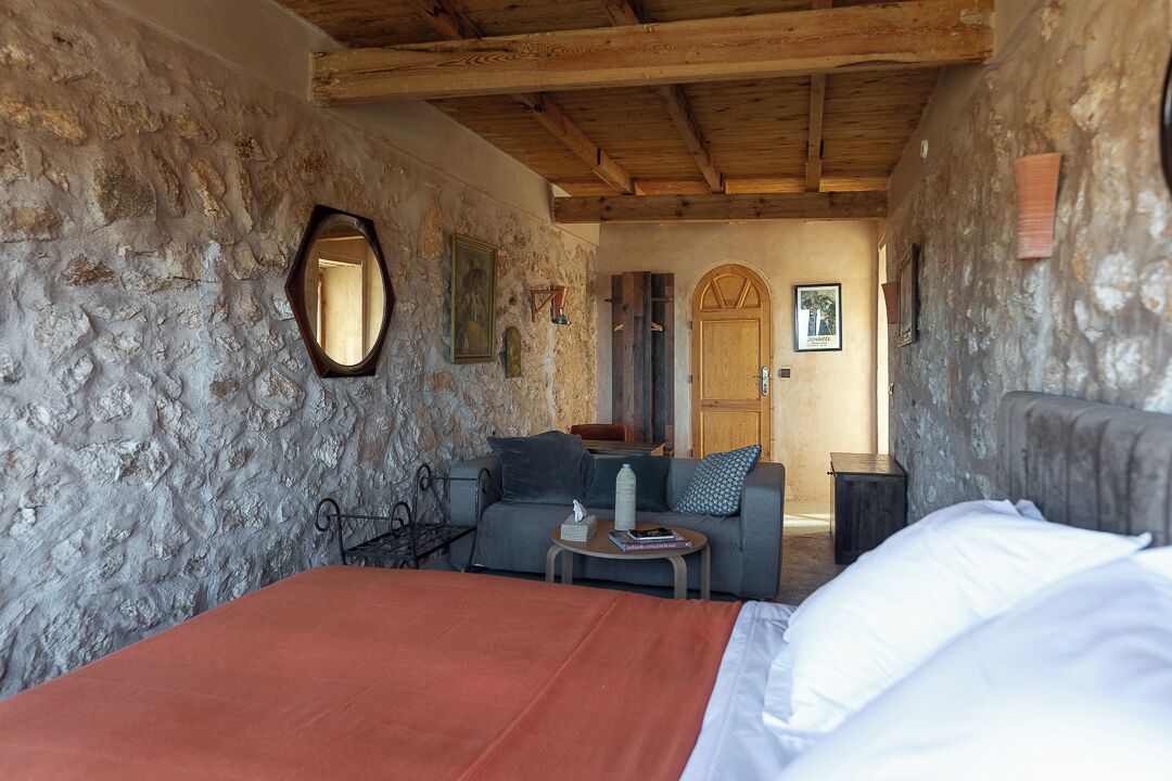 A rustic room with stone walls, a wooden ceiling, a bed, a sofa, and a small table with a book.