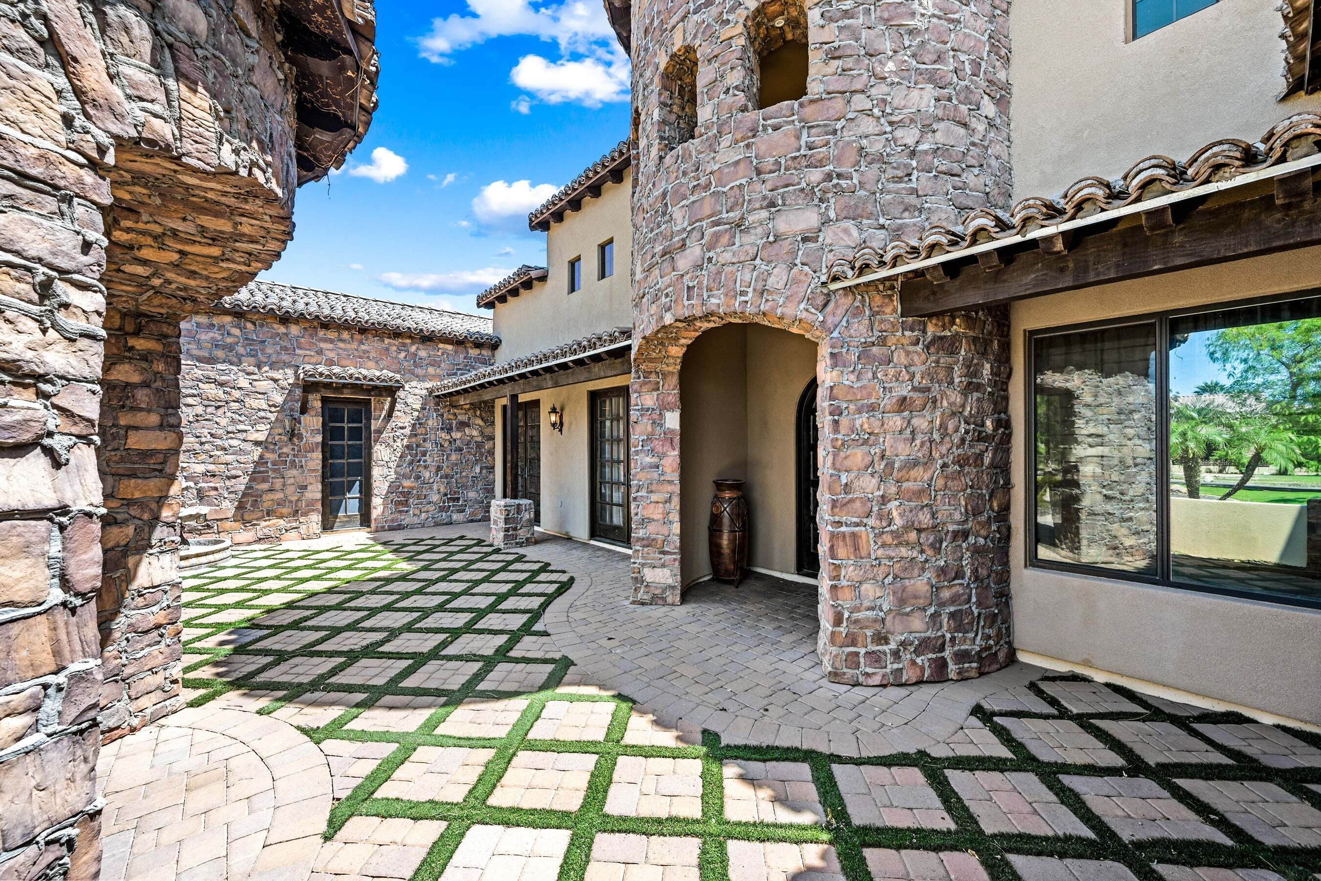 A courtyard with stone walls, a tiled roof, and a paved area with a geometric pattern.