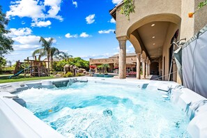 A hot tub area with a pool, palm trees, and a building with arches.