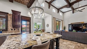A spacious kitchen with a granite island, dark wooden cabinets, and a ceiling fan. - Luxury 6BR Mesa Estate | Pool, Water Slide, Pickleball, Theater (Mesa)