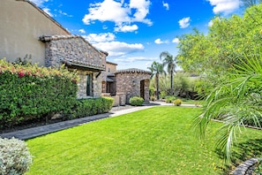 A well-maintained garden with a stone building, a clear sky, and a variety of plants.