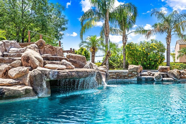 A pool with a waterfall feature surrounded by rocks and palm trees.
