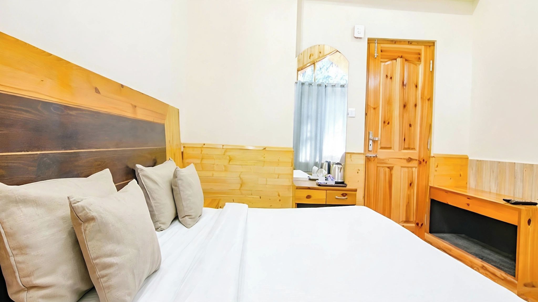 A bedroom with a wooden headboard, a bed with white linens, a wooden dresser, and a wooden door.