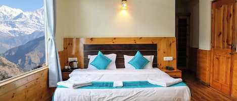 A bedroom with a wooden headboard, a bed with white bedding and turquoise pillows, a nightstand with a lamp, and a view of mountains through a window.