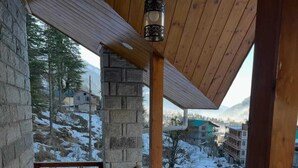 Un balcón de madera con pilares de piedra, barandilla de metal y un farol colgante.