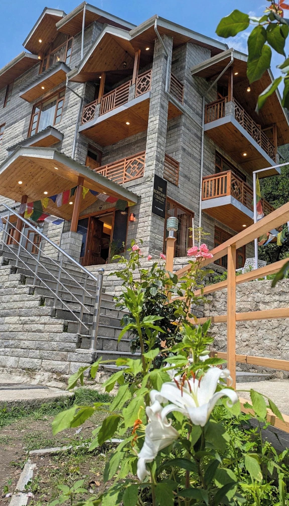 A multi-story building with stone walls and wooden balconies, featuring a staircase leading to the entrance.