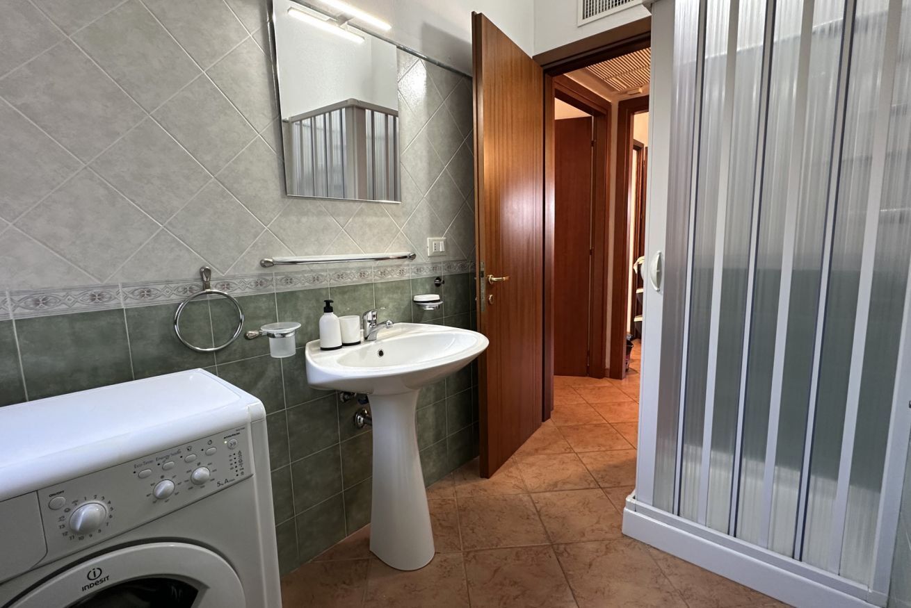 A bathroom with a washing machine, sink, and a shower area.