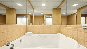 Ein Badezimmer mit einer großen Badewanne, gefliesten Wänden und Spiegeln.