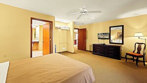 Una habitación de hotel con cama, cómoda, silla, ventilador de techo y espejo.