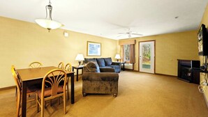 Habitación de hotel con una mesa de comedor, sillas, un sofá, un televisor y un ventilador de techo.