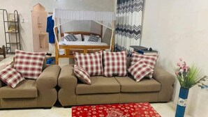 Ein Wohnzimmer mit zwei Sofas, einem roten Couchtisch, einem Bett mit Baldachin und einer Wand mit gemusterten Vorhängen.