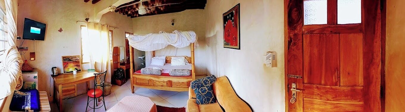 A bedroom with a wooden bed, a desk, a chair, and a television.