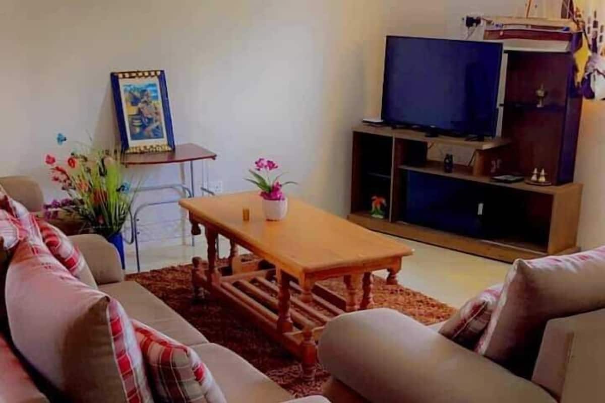 A living room with a sofa set, a coffee table, a television, and a small table with a picture frame and flowers.