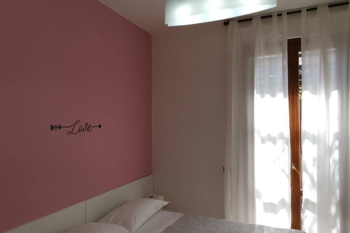 Ein Schlafzimmer mit einem Bett, einer rosa Wand und einem Fenster mit durchsichtigen Vorhängen.